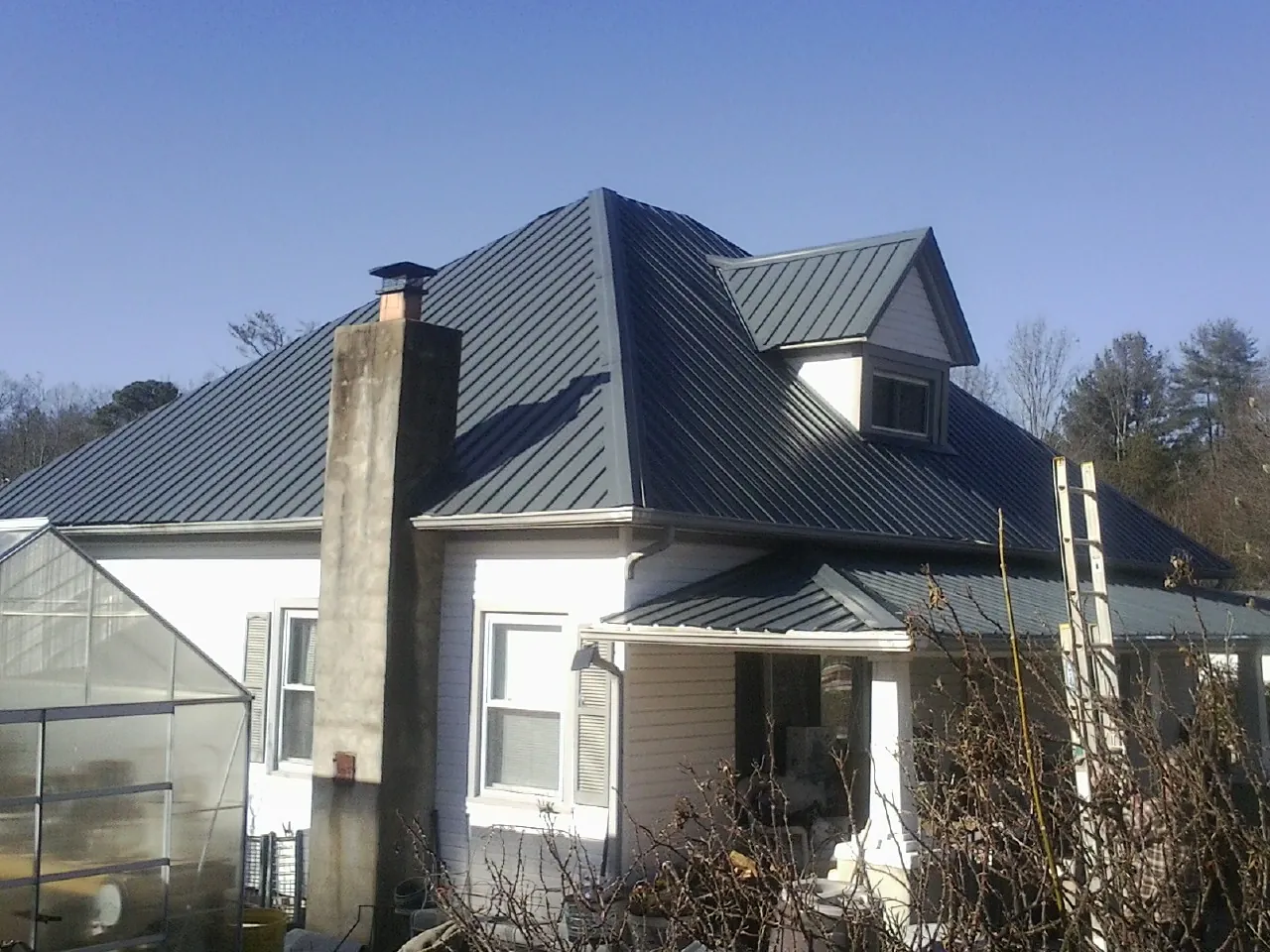 Dark blue standing seam metal roof on a white farmhouse with dormer — Slate & Tile Roof Repair by Roofing Brothers in Spring Grove