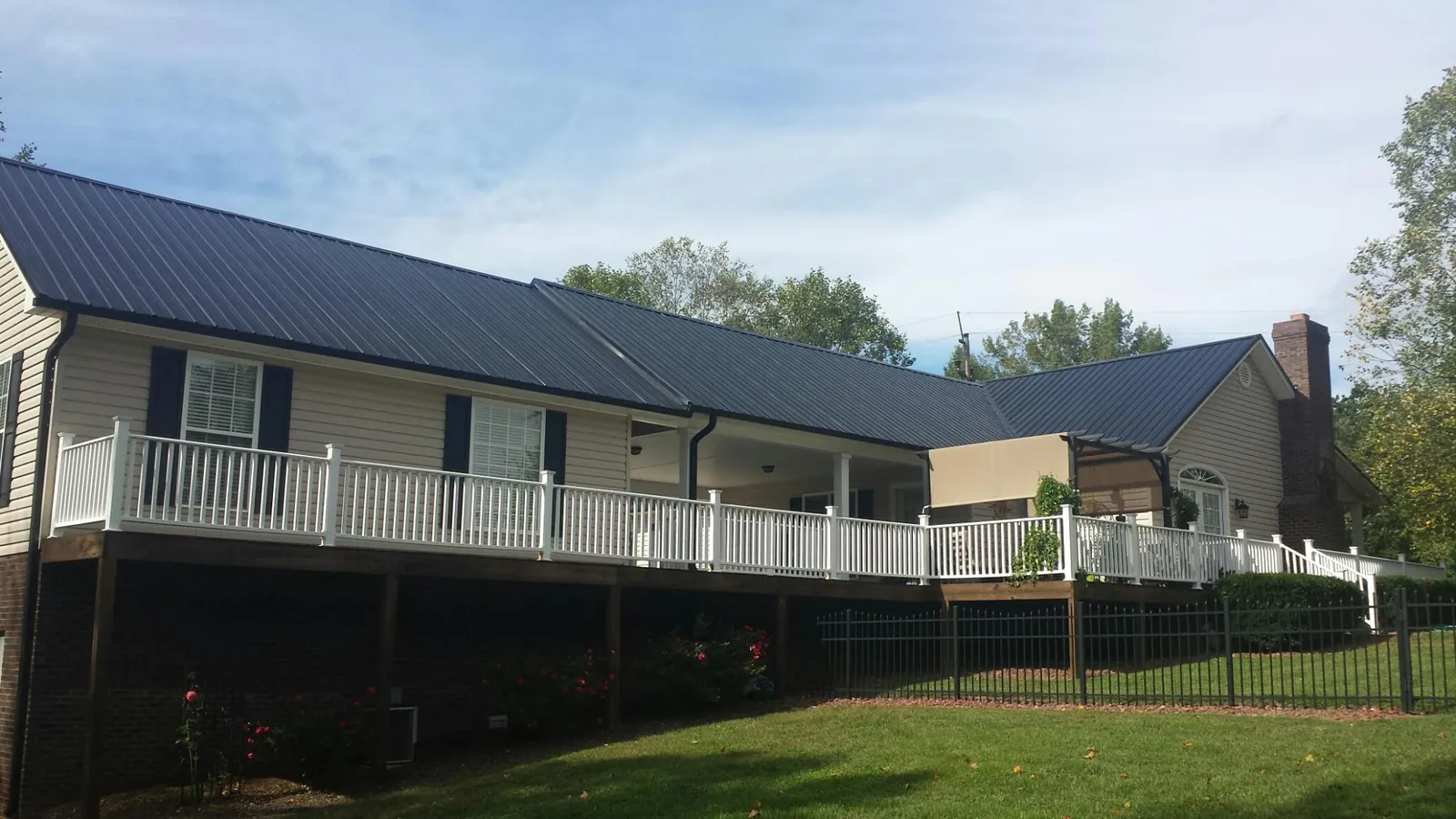 Black metal roof above a long white railed deck on a hillside home in Spring Grove